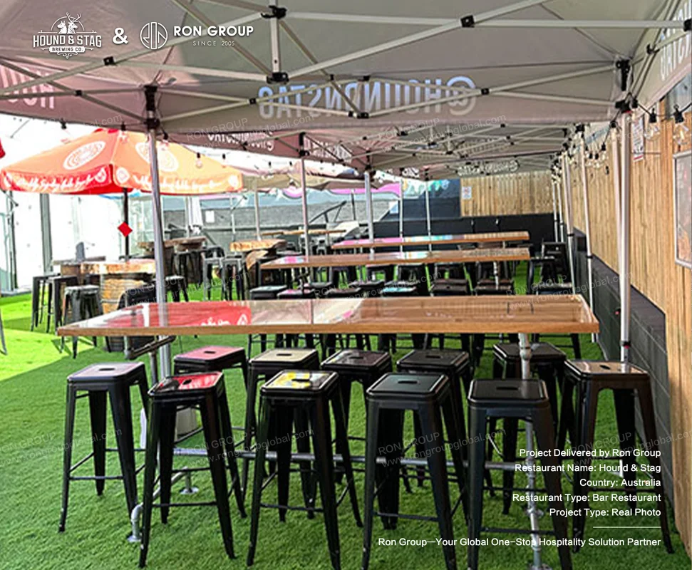 Hound Stag outdoor bar seating area with canopy long wooden tables black stools and turf