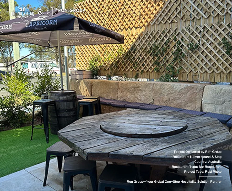 Hound Stag outdoor wooden table with black stools branded umbrella stone wall and greenery