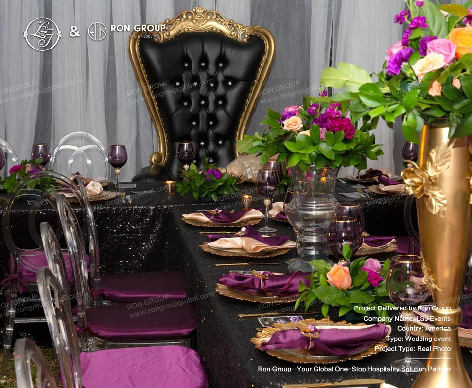 Black and purple wedding table decor with black sequined tablecloth, purple napkins, gold-rimmed glassware, floral centerpiece, and black gold throne chair