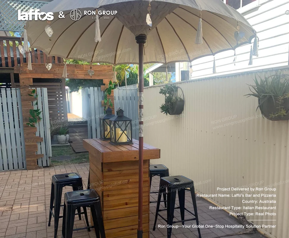 Laffos Bar and Pizzeria outdoor wooden bar with black stools beige umbrella potted plants and rustic patio