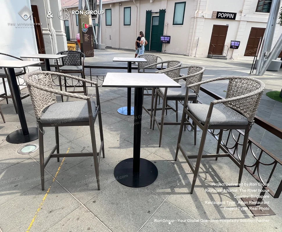 Riverhouse outdoor dining setup with high tables black metal bases woven chairs and colonial buildings
