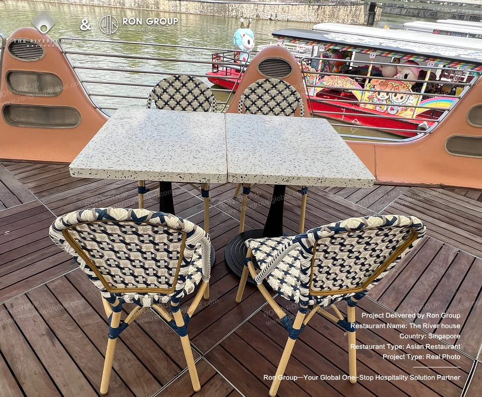 Riverhouse outdoor dining setup on deck with terrazzo tables woven rope chairs and river boats