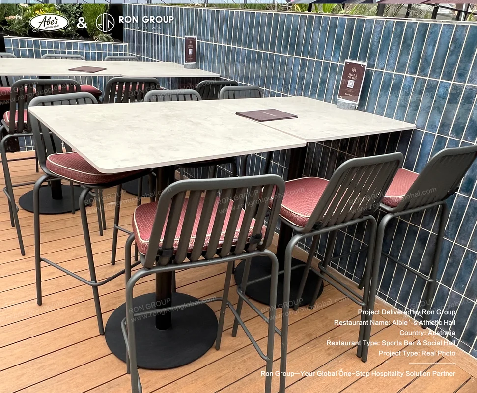Outdoor timber deck with marble-top tables red-cushioned metal chairs and blue tiled wall