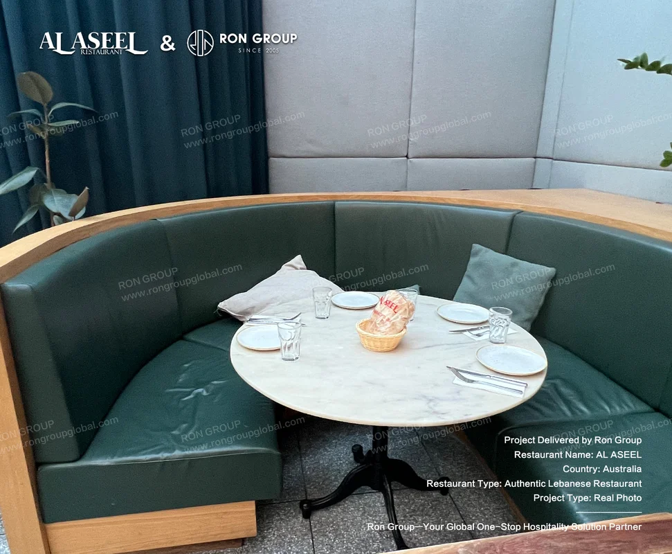 Curved deep green leather booth with round marble table set for dining at Al Aseel