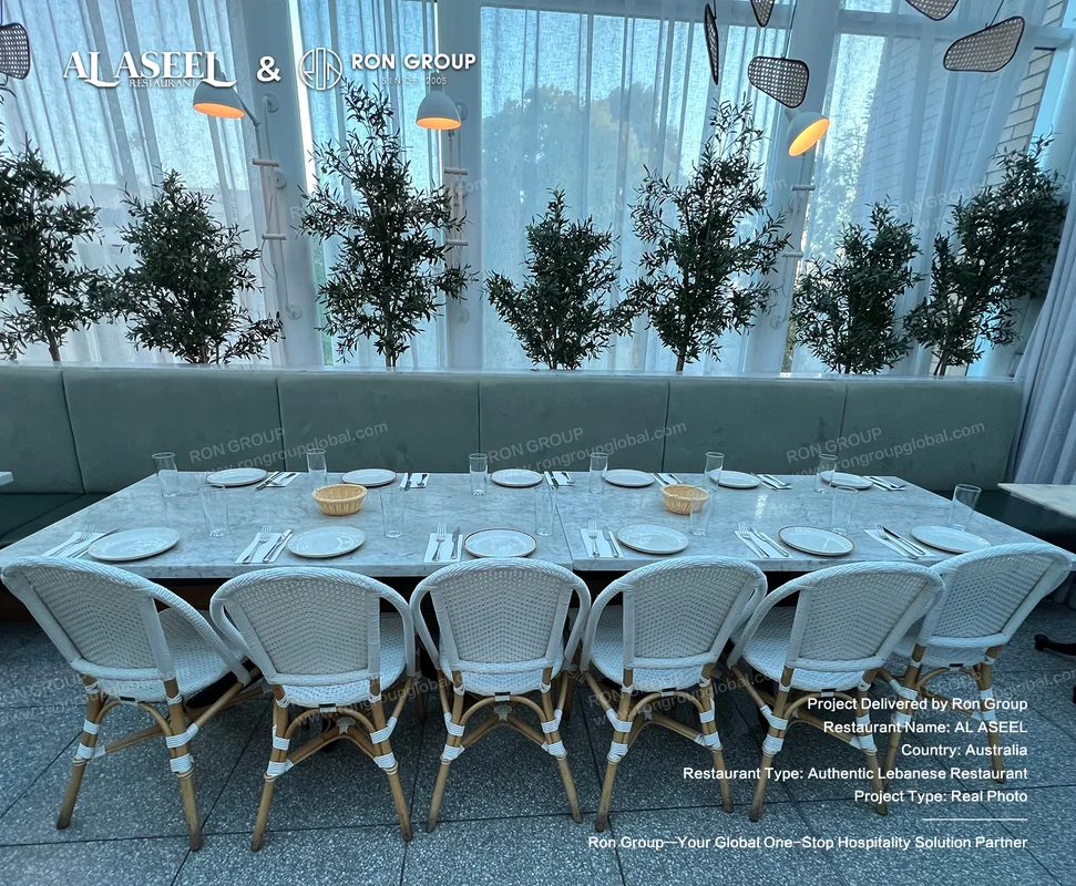 Eight-seater long white marble dining table with woven armchairs and potted plants at Al Aseel