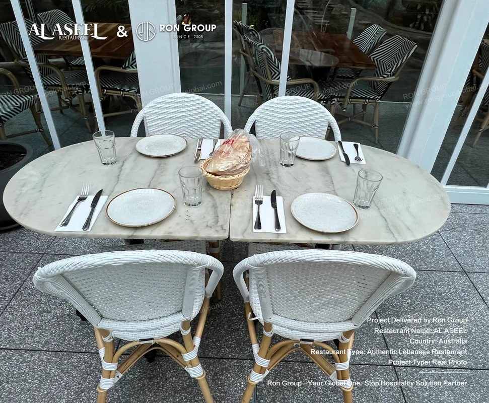 Four-seater marble patio table with white woven chairs and full tableware setting at Al Aseel