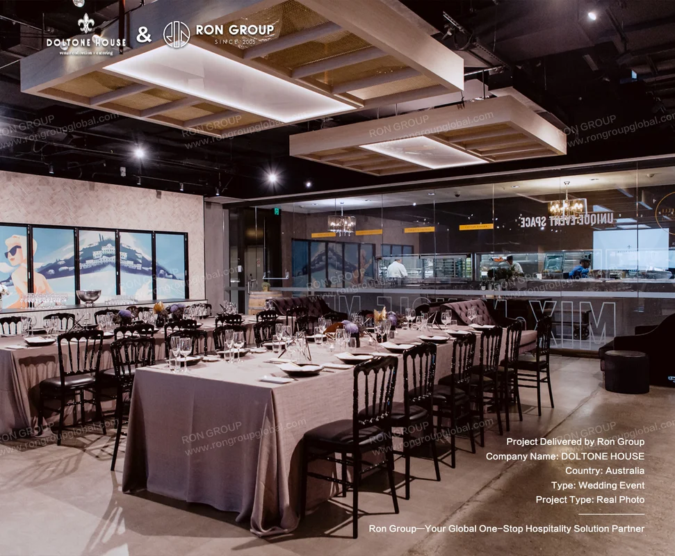 Modern event dining hall with grey linen long tables black chiavari chairs and geometric ceiling lights