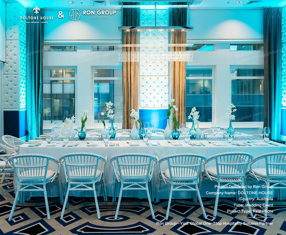 Waterfront banquet room with light blue woven chairs and blue floral table styling