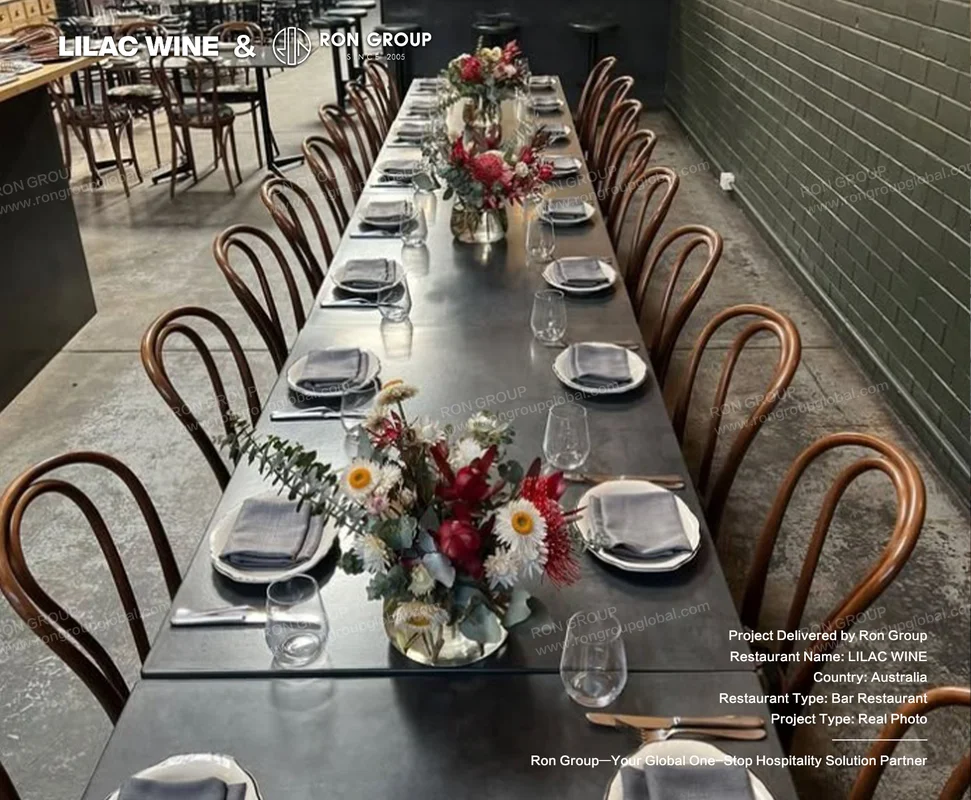 Long black communal dining table with wooden bentwood chairs and white ceramic plates