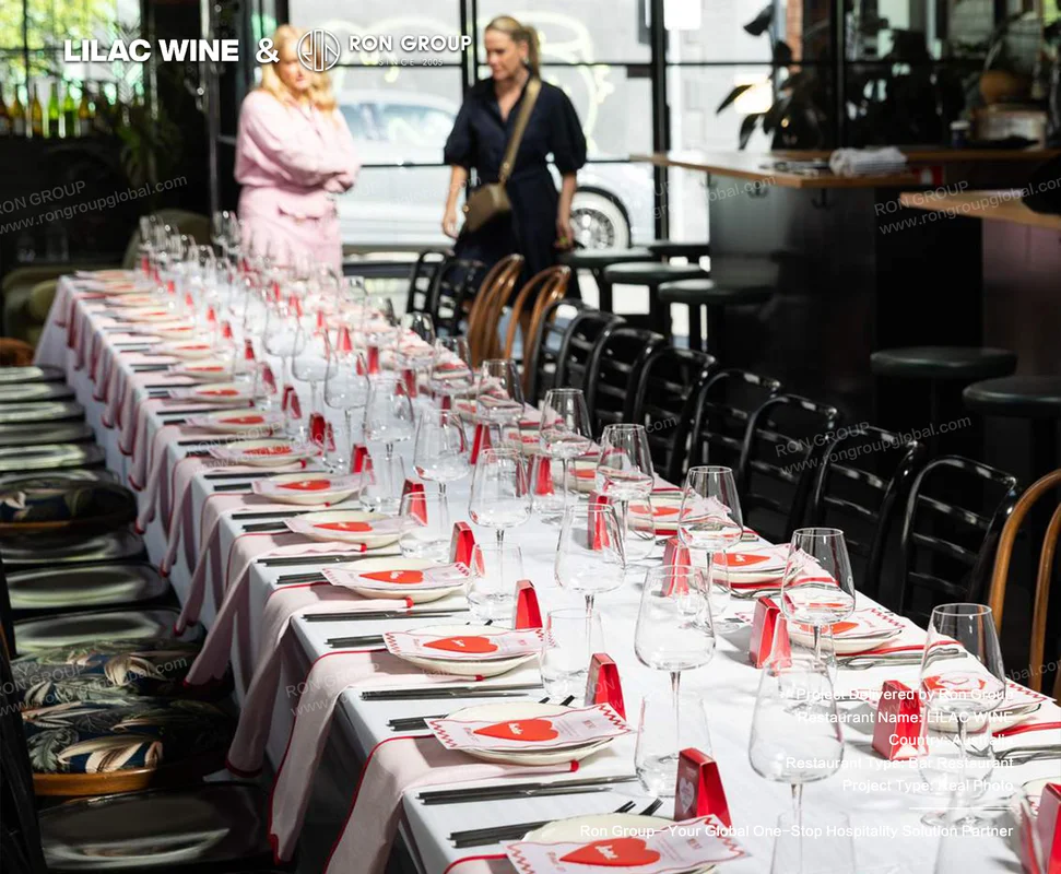 Long white-linen banquet table set with crystal wine glasses and bentwood chairs at Lilac Wine