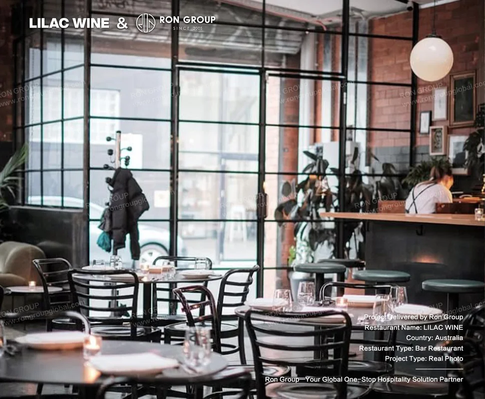 Round bistro tables with black chairs beside industrial metal and glass partitions at Lilac Wine