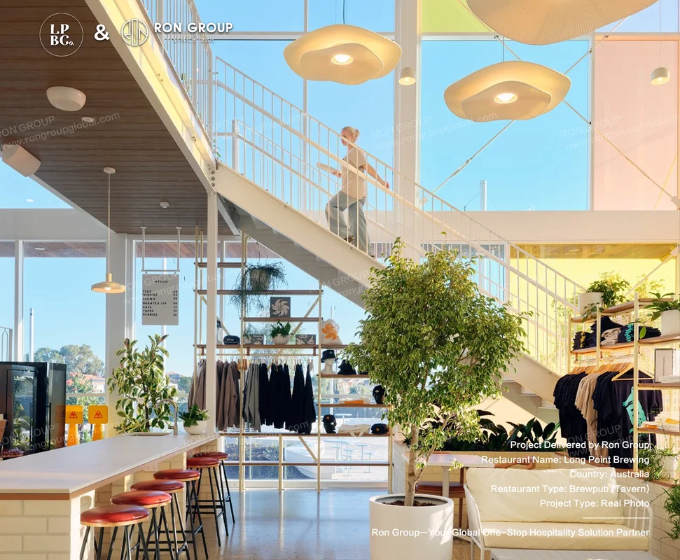 Double-height atrium at Long Point Brewing with white staircase indoor tree and red bar stools