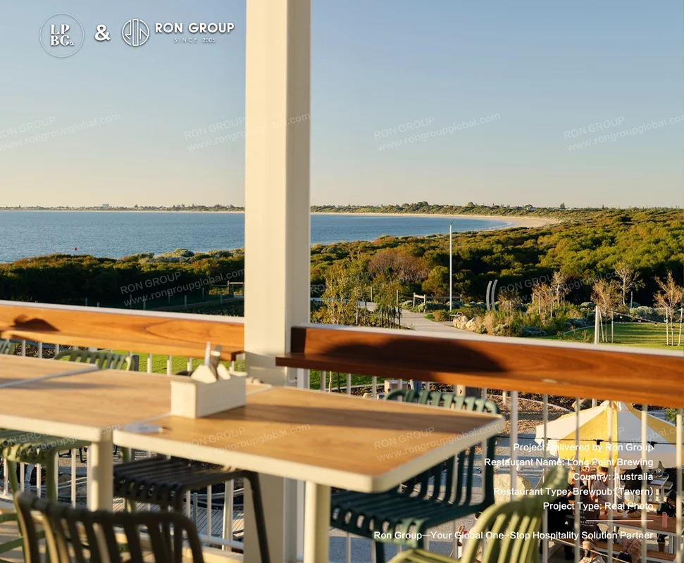 Oceanfront outdoor dining deck with wooden tables and green coastal chairs overlooking Kennedy Bay