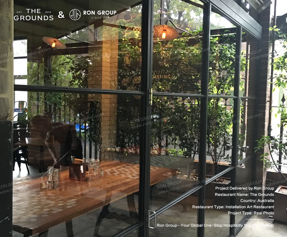 Glass door entrance framed in black steel with artistic etchings and suspended greenery at Sydney Garden Restaurant