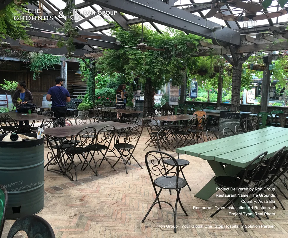 Covered outdoor dining pergola with lush hanging greenery, timber picnic tables, and metal dining chairs at Sydney Garden Restaurant