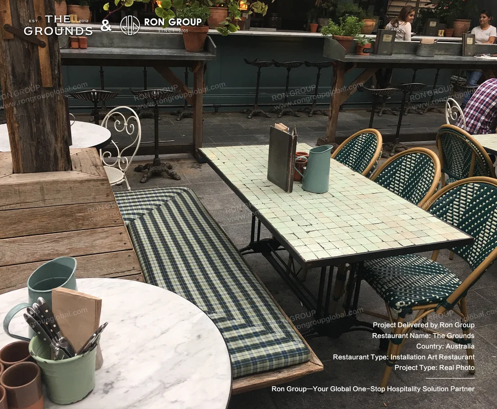 Long communal mosaic dining table with green woven chairs and cushioned bench seating at Sydney Garden Restaurant