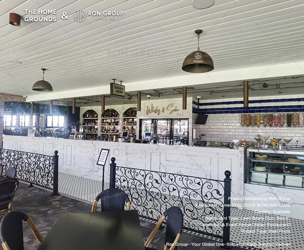 White marble bar counter with ornate black iron railing and blue tile backdrop at The Home Grounds
