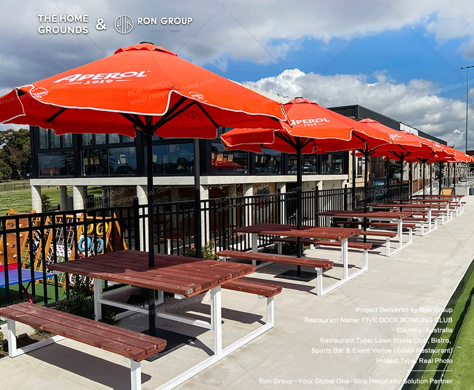 The Home Grounds Five Dock outdoor lawn patio with timber picnic tables and orange umbrellas
