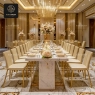 A grand dining hall with a long marble table, velvet chairs, and elegant chandeliers.