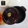A dark red enamel cast iron dutch oven with a lid resting beside it.