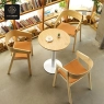 Three Nordic solid wood chairs with a round table in a cozy, book-lined room.