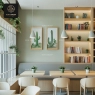 A cozy cafe interior with light wood tables, cushioned bench seating, and cactus art.