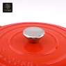 A close-up view of the metal knob and 'Success' embossed on the orange dutch oven lid.