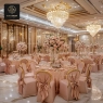 A formal dining hall with large chandeliers and pink-draped chairs.