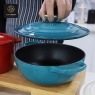 A person's hand lifting the lid off a blue enamel cast iron dutch oven.