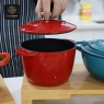 A person's hand is shown lifting the lid of a red, pumpkin-shaped enamel pot.