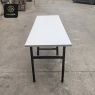A white rectangular folding banquet table with a black metal frame, set outdoors on concrete.