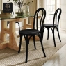 Two black classic bentwood chairs at a wooden dining table.