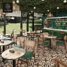 A busy restaurant scene with multiple mosaic tables, green chairs and plants.