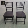A pair of black wooden Chiavari chairs with black cushions.