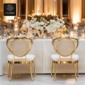 Two elegant gold-framed chairs with white seats, at a table with floral decor.