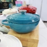 A close-up of a person's hand lifting the lid of a light blue, heart-shaped pot.