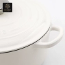 A close-up view of the metal knob and 'Success' embossing on the white dutch oven lid.