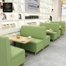 Dining area with light-green booths, tables, and white shelves in the background.