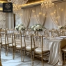 A banquet hall with gold chairs and long tables decorated with white bouquets.