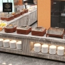 A modern buffet setup featuring multiple chafing dishes on elegant wooden bases and stacks of plates.