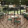 A cafe setting with mosaic tables and green chairs, with leafy decor overhead.