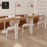 A chic cafe featuring an extended channel-tufted sofa, light chairs with unique frames, and a white backdrop.