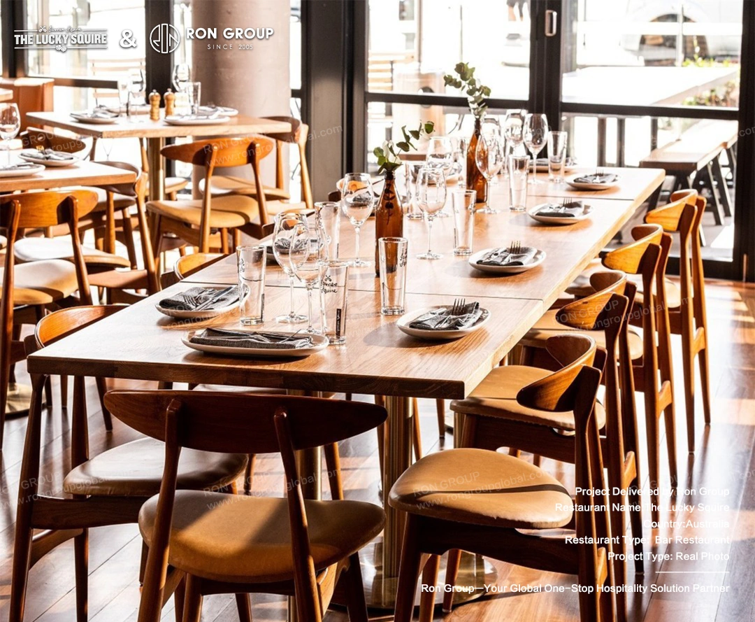 Long wooden dining table set up with custom James Squire glasses, plates, and ergonomic wooden chairs