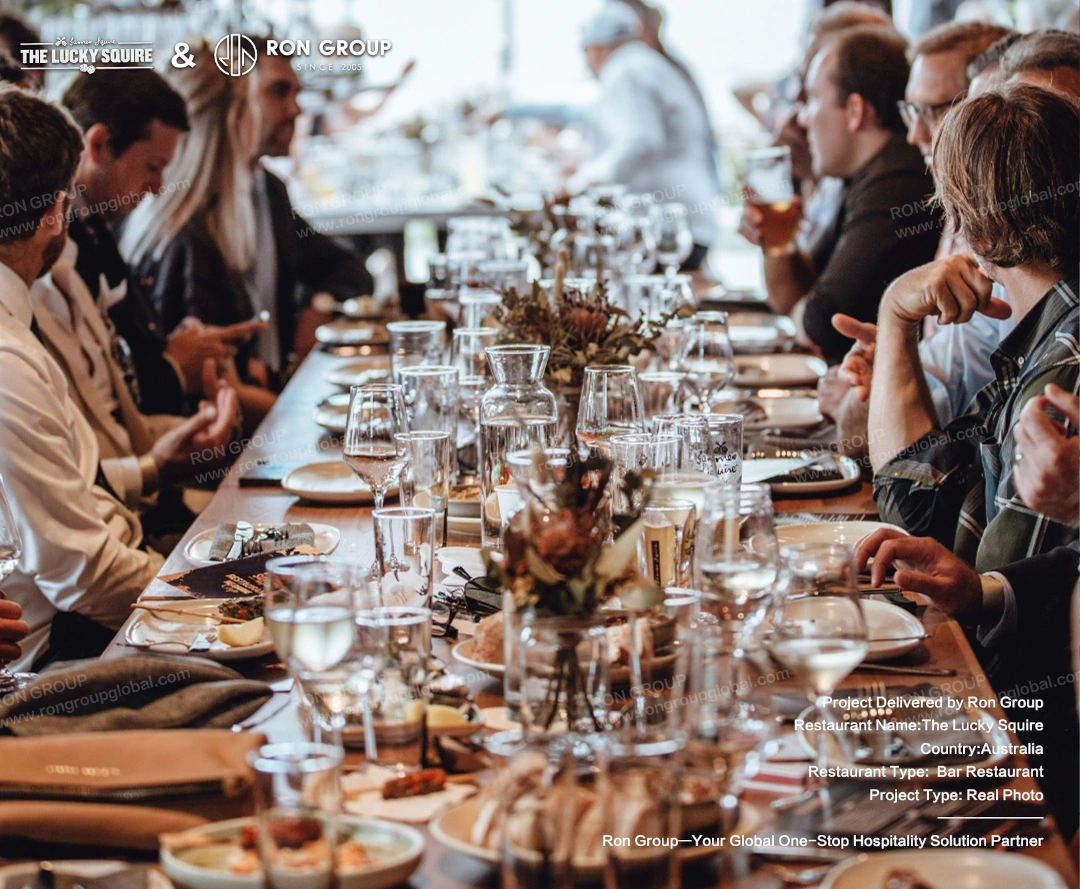 Guests enjoying drinks and meals at a long table, showcasing the furniture in a busy commercial environment