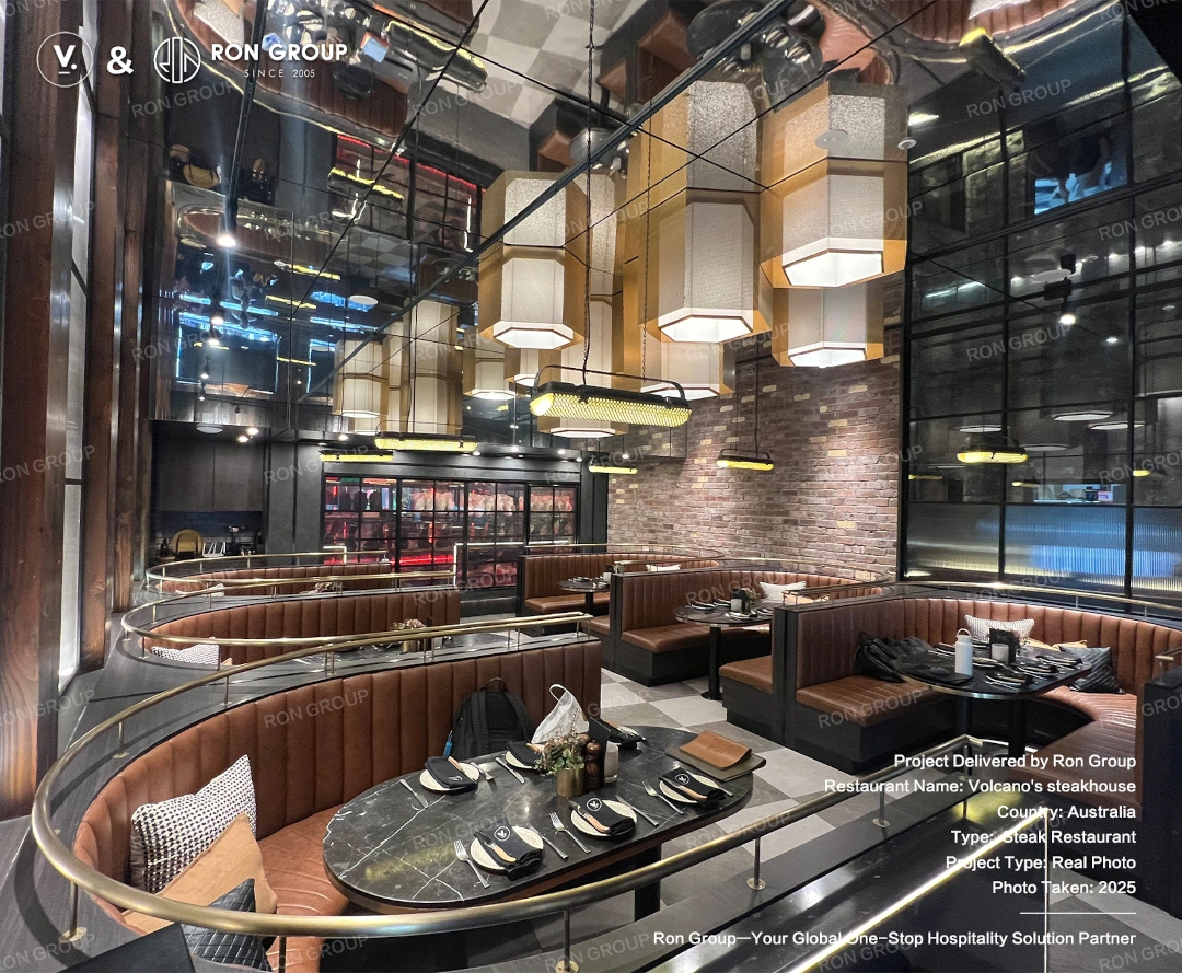 Completed upscale booth area at Volcano's Steakhouse Curved booth seating, dark marble-look tabletops, and statement pendant lighting in a premium steakhouse lounge area