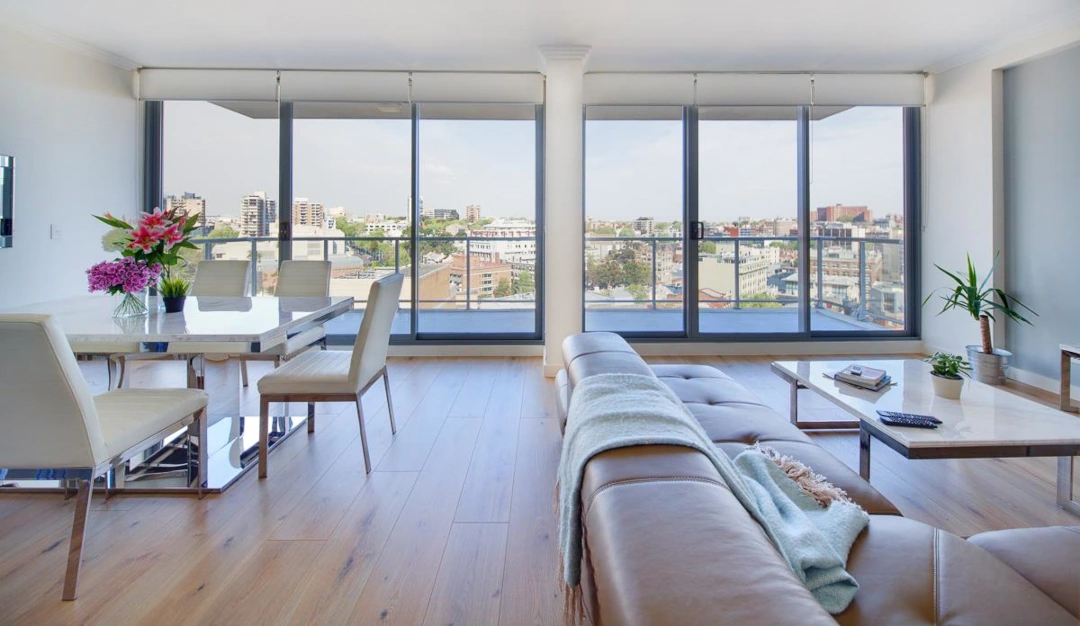 A bright open-plan living and dining area in a city-view residence, featuring premium leather furniture, marble tables, and panoramic views of Sydney.
