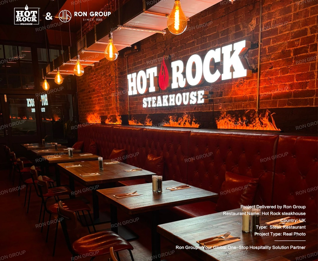 Warm Steakhouse Dining Atmosphere A warm night-time view of Hot Rock Steakhouse with red leather booths, dark wooden tables, fire feature walls, and glowing pendant lights.