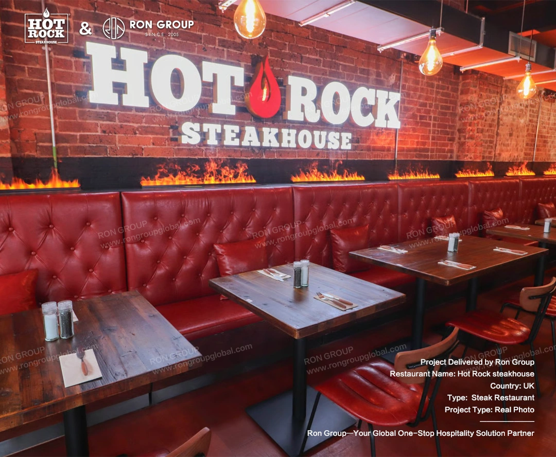 Red Leather Booths and Wooden Dining Tables A close view of Hot Rock Steakhouse dining tables, red leather booth seating, red leather dining chairs, brick wall, and fire feature details.