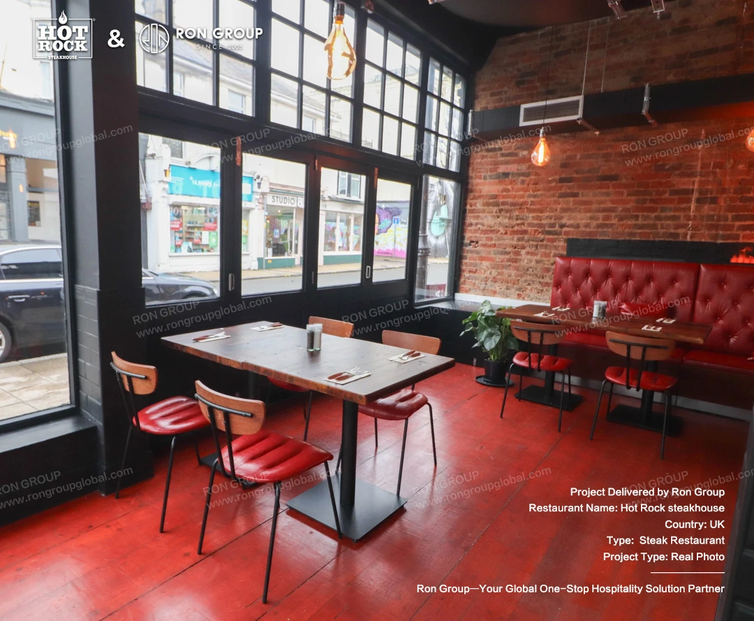 Window-Side Dining Area with Red-Themed Seating A window-side dining area at Hot Rock Steakhouse with red leather chairs, wooden tables, red flooring, brick walls, and booth seating.