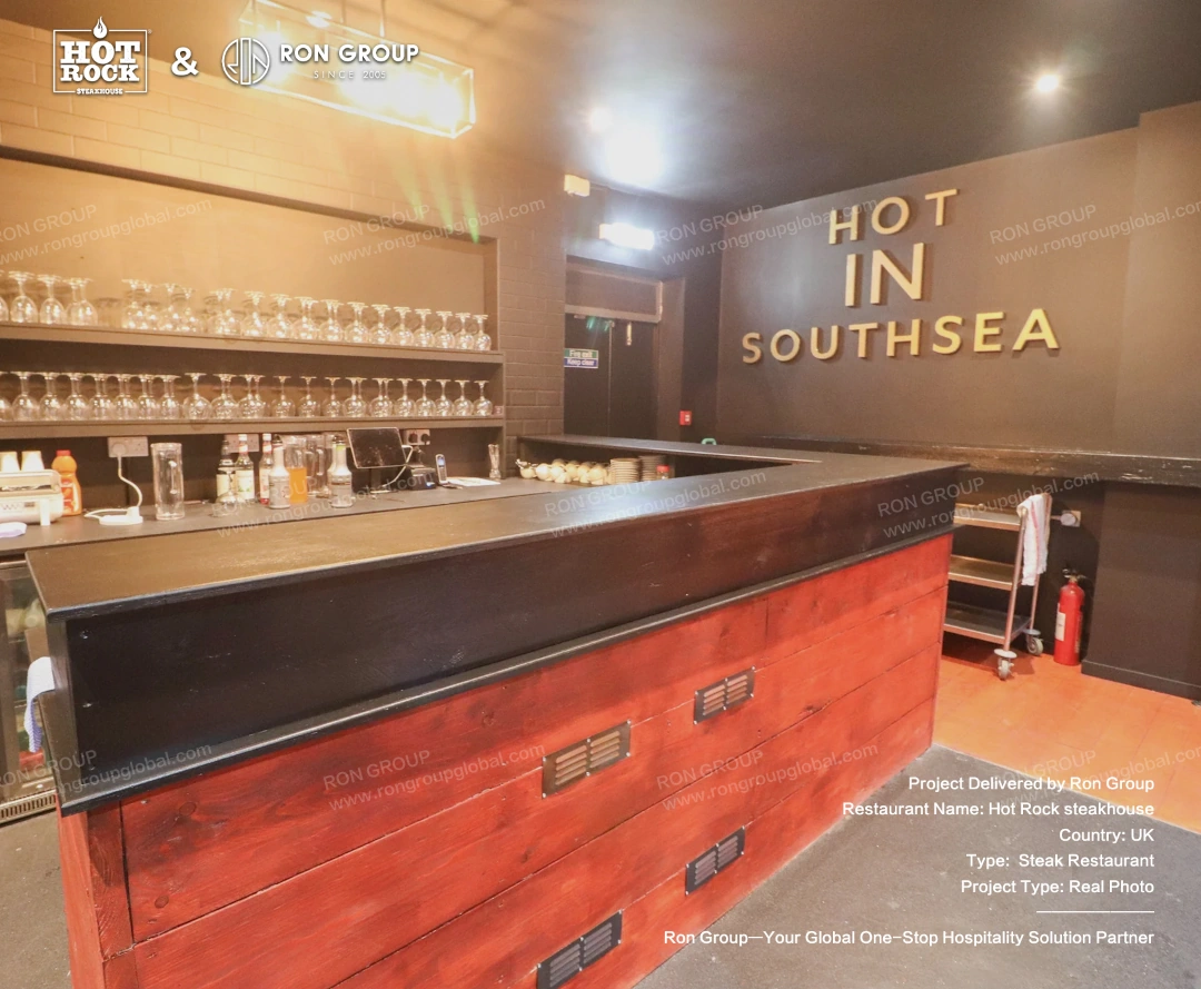Hot Rock Steakhouse Bar Area Hot Rock Steakhouse bar area with dark counter finishes, glassware shelving, warm lighting, and Southsea wall signage.